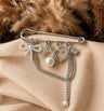 Broche plateado con dijes y perlas